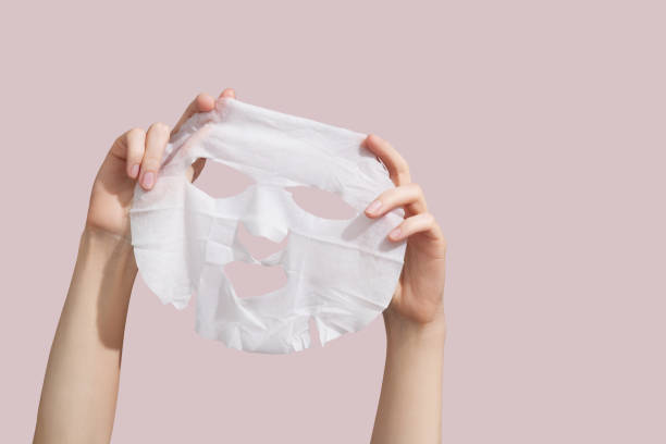 Female hands holding sheet of white mask on pink background. High quality photo